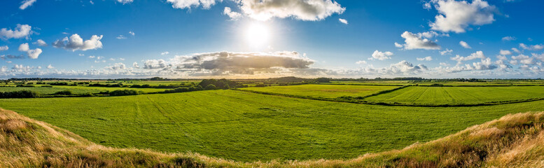 Panoramafoto über den Ringwall der Lembecksburg auf der Nordseeinsel Föhr mit Naturgras, Sonne, grünen Feldern und aufgelockerter Bewölkung am Horizont