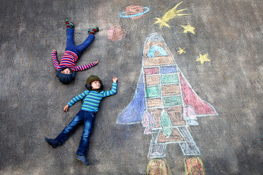 Two funny little kid boys flying into space on a chalk drawn space shuttle. Creative outdoor summer leisure for children. Real life, real people, imagination and joy. Child dreaming to be austronaut