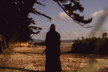 A samurai in black kimono is walking through forest.