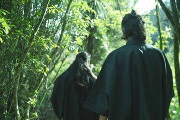 A samurai in black kimono is walking through forest.