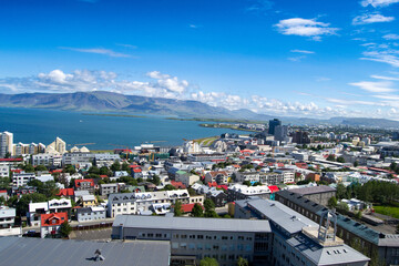 A view of the colorful rooftops of houses in Reykjavik. The narrow streets and pedestrian paths create a cozy atmosphere. The ocean and mountains are visible in the background.