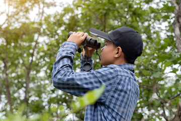 Fototapeta premium Young man with binoculars exploring the forest on a sunny day, enjoying outdoor adventure and wildlife observation.