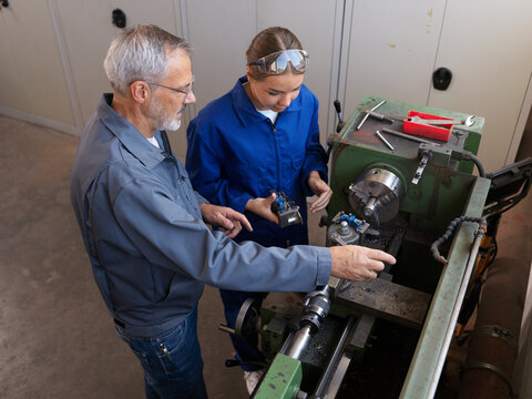 Instructor giving lathe machine training to apprentice at workshop