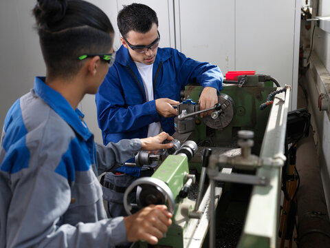 Teenage apprentices using lathe machine at workshop