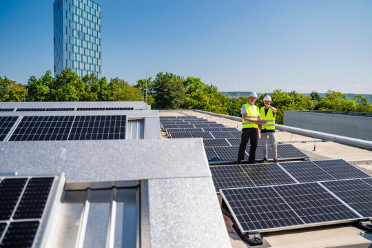 Two technicians using tablet PC on the roof of a company building with solar panels