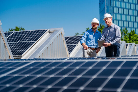 Two businessmen wearing hardhats having a meeting on the roof of a company building with solar panels