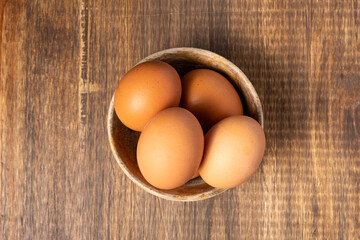 Brown chicken eggs inside a wooden bowl and on a wooden table, viewed from above.
