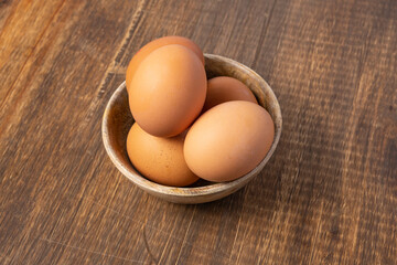 Brown chicken eggs inside a wooden bowl and on a wooden table, viewed from above.