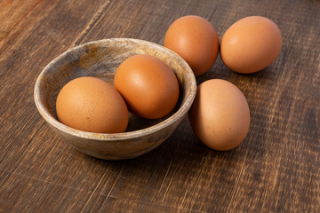 Brown chicken eggs inside a wooden bowl and on a wooden table, viewed from above.