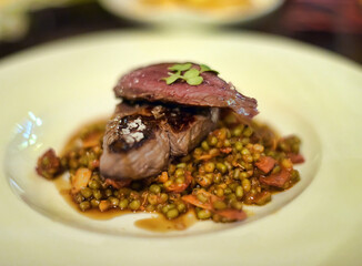 An elegant restaurant presentation of a juicy piece of tender-roasted beef, laid on top of a side dish of green beans and vegetables in a fragrant sauce.  