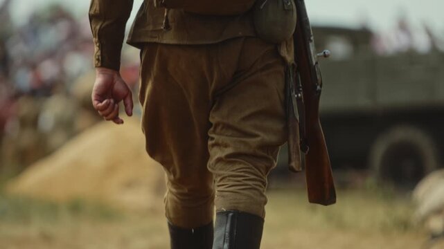 Soviet soldier of Red Army with Mosin rifle walks through field before battle simulation of Great Patriotic War. Infantryman wears in jackboots, kirza yuftev boots, duffel bag, kit bag, helmet ssh-40
