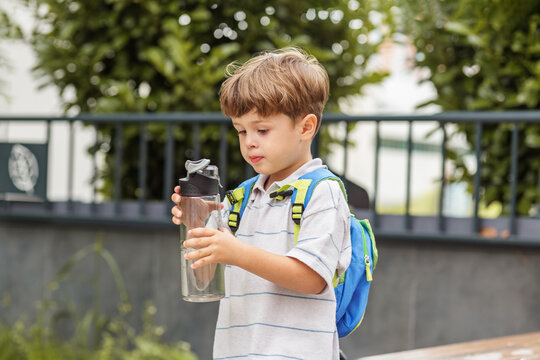 Kid boy examining water bottle outdoors. Back to school