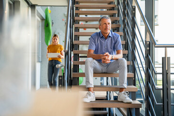 Contemplative businessman sitting on staircase with colleague using tablet PC in office