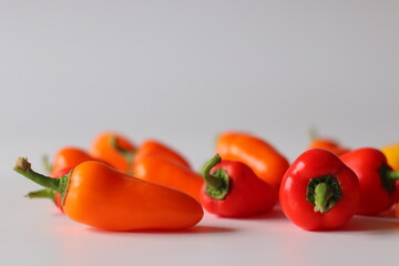 Mini bell peppers presented on a white surface, featuring vibrant red, orange, and yellow pods with green stems