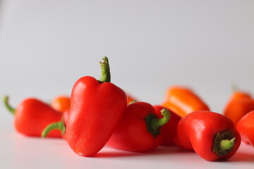 Mini bell peppers presented on a white surface, featuring vibrant red, orange, and yellow pods with green stems