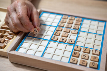 closeup hands carefully placing number into Sudoku puzzle, senior man focused on solving puzzle on wooden board, Brain exercise, cognitive health, and mental agility in mature age, brain health