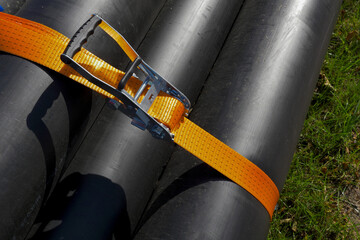 Close-up of black plastic pipes secured with an orange ratchet strap for transportation or storage. Industrial equipment and safety concept.