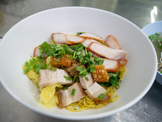 Chinese egg noodles with roasted red pork, crispy pork belly, and wontons in a bowl on table.