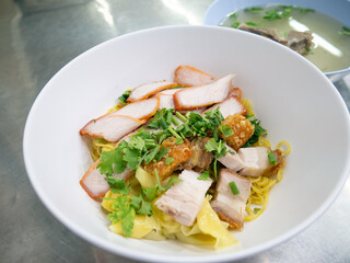 Chinese egg noodles with roasted red pork, crispy pork belly, and wontons in a bowl on table.