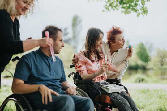 Friends and caregivers engage in outdoor activities, promoting togetherness and joy, as people of all abilities participate in a playful bubble-blowing session in a lush, green park environment.