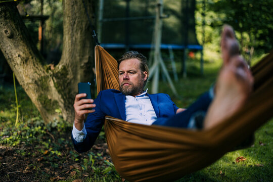 Mature businessman using smart phone and lying in hammock at park
