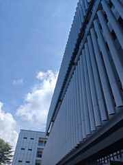 Modern architectural building facade with vertical metal panels, captured against a bright blue sky and scattered clouds.