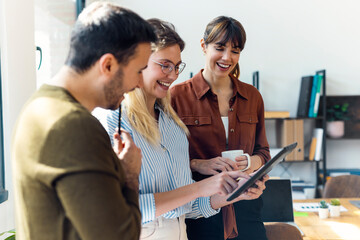 Happy businesswoman using tablet PC and discussing ideas with colleagues in office
