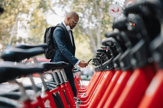 Businessman renting bicycle through smart phone at street