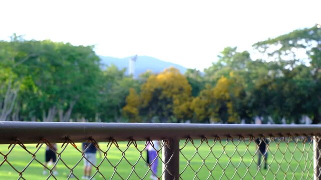 A group of people are playing a game of baseball on a field. The fence surrounding the field is made of metal and has a chain link design