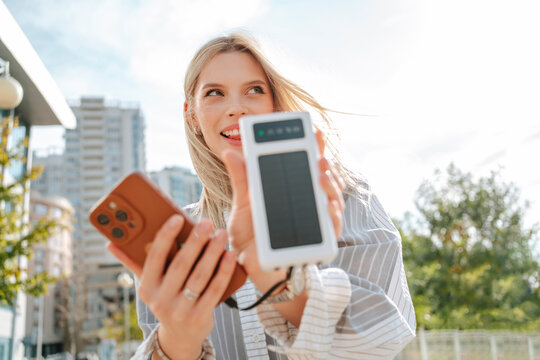 Young woman charging smart phone with solar power bank