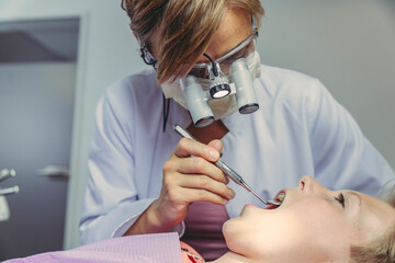 Denist examining boy's teeth, using head magnifiers and dental instrument