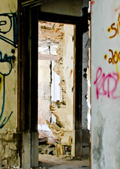 An interior view of a dilapidated building, with a doorway revealing the destruction of the wall.