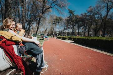 Obraz premium A mother sits on a bench with her two children on a bright sunny day in a peaceful park, surrounded by nature.