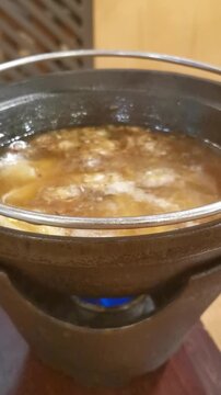 A wok of hot rawon simmers slowly on a clay stove, savory broth bubbling within. A slow food concept