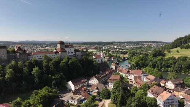 Drone aerial of Aarburg castle, historic old town and Aare river in Canton Solothurn, Switzerland, surrounded by lush green hills and scenic landscapes.