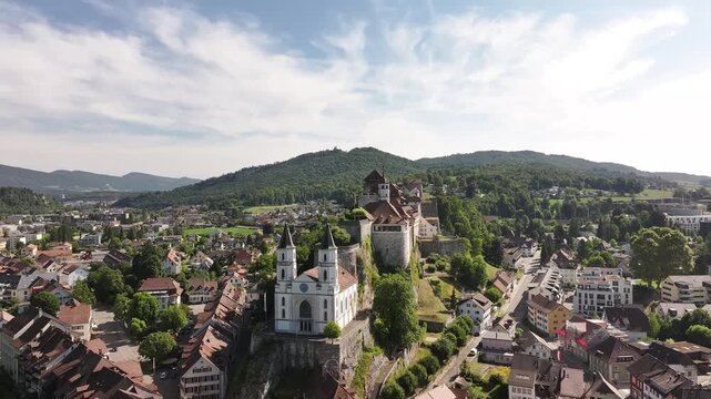 Aarburg castle, church and old town along Aare river in Canton Solothurn, Switzerland, aerial drone view with scenic green hills in background.