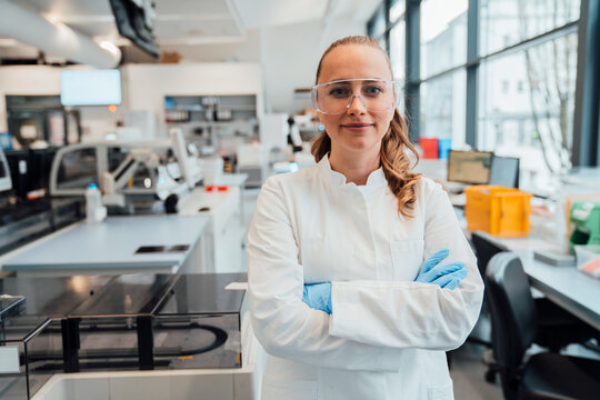Scientist with safety glasses in modern laboratory crossing arms