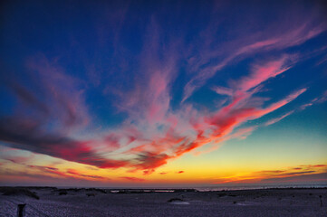 Żywe, tańczące chmury rozciągają się po niebie, malując wspaniały zachód słońca nad spokojną plażą. © Pol Badger
