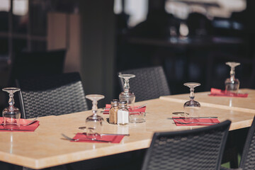 Elegant outdoor dining setup featuring neatly arranged tables with glasses and condiments near a sunlit window in a vibrant restaurant atmosphere