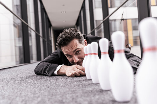 Mature businessman keeping bowling pin in row on floor at work place