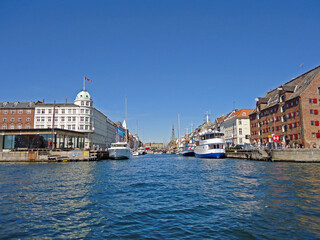 The bustling river flowing through Copenhagen, Denmark, on a bright, sunny day. Historic buildings line the waterfront, with boats and ferries navigating the scenic waterway.
