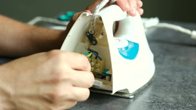 Precision focused technician repairing internal electrical components of disassembled iron, carefully analyzing technical details and potential wiring issues in professional workshop setting