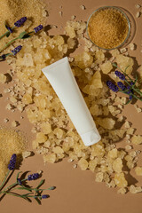 Tube of beauty cream placed diagonally over sugar and lavender, suggesting the freshness of spa body scrubs. Top view, space for design