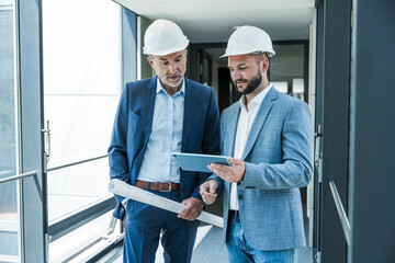 Architects with safety helmets collaborating on tablet at modern office