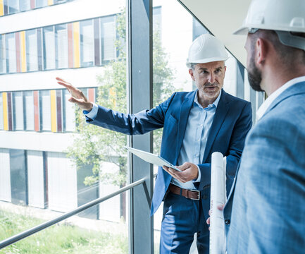 Architects in safety helmets discussing project with tablet in office
