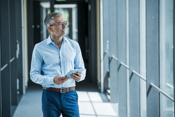 Business professional with tablet looking out window in modern office