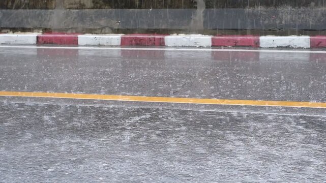 The road is wet and has a yellow line painted on it. The rain is coming down in sheets, making the road slick and difficult to navigate. The yellow line serves as a guide for drivers