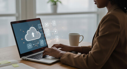 Person using a laptop with cloud storage interface and a mug on the desk near a bright window