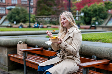 Smiling businesswoman eating takeaway lunch sitting at park