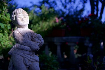 Estatua de piedra enfocada con fondo de plantas desenfocado y un haz de luz en diagonal. 